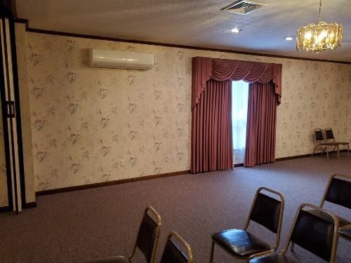 Empty banquet hall with floral wallpaper, mauve curtains, and rows of chairs on a carpeted floor