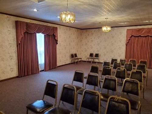 Empty meeting room with rows of chairs, red drapes, patterned wallpaper, and ceiling lights