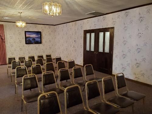 Empty meeting room with rows of chairs, floral wallpaper, ceiling lights, and a wall-mounted TV