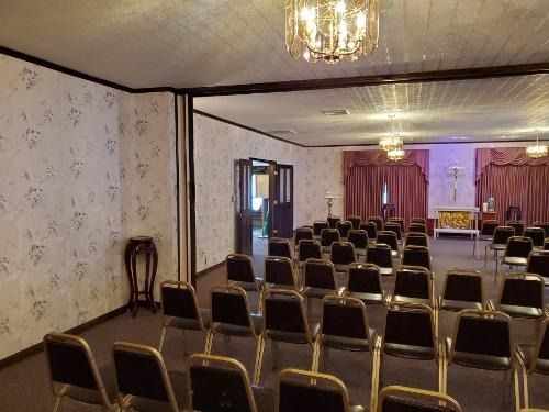 Empty banquet hall with rows of chairs facing a small stage, chandeliers, and purple curtains
