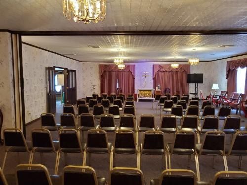 Empty banquet hall with rows of black chairs facing a lit stage and purple curtains