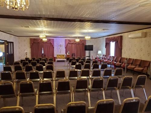 Empty banquet hall with rows of chairs facing a curtained stage and tables along the sides