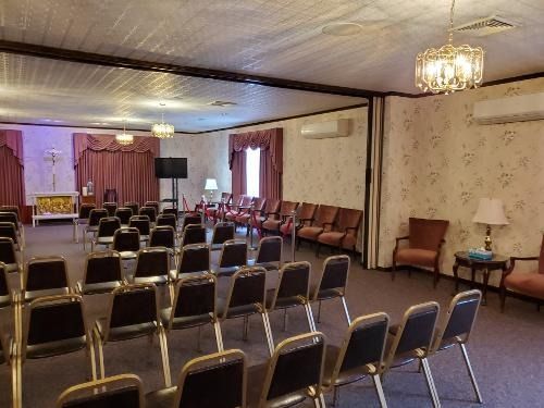 Empty event hall with rows of chairs facing a small stage and podium under chandeliers