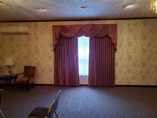 Empty room with mauve drapes, floral wallpaper, carpet, and a small seating area by the wall