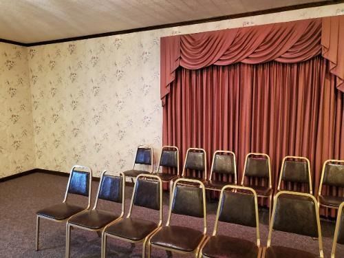 Rows of empty chairs in a small room with pink curtains and patterned wallpaper.