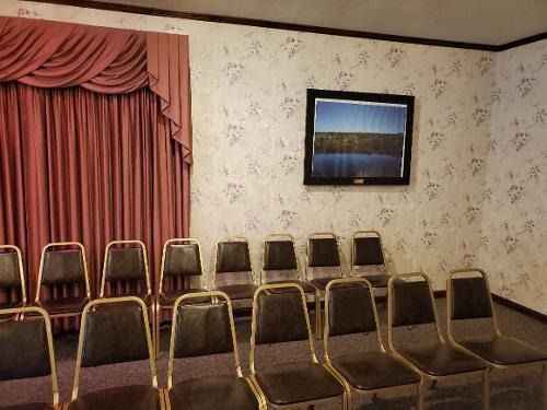 Empty chairs in a small room with floral wallpaper, pink curtains, and a framed landscape on the wall.