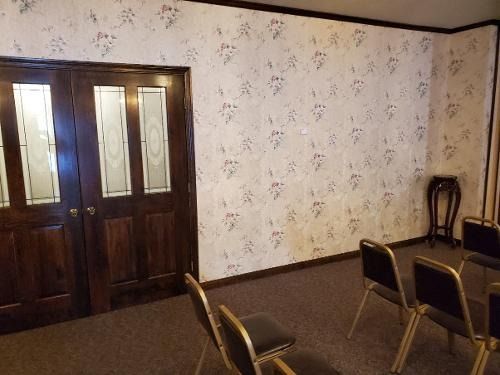 Small meeting room with wooden double doors, floral wallpaper, and several chairs around a table.