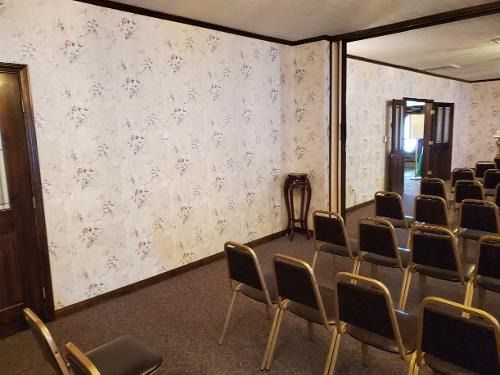 Empty meeting room with rows of brown chairs, a small table, patterned wallpaper, and mirrored walls