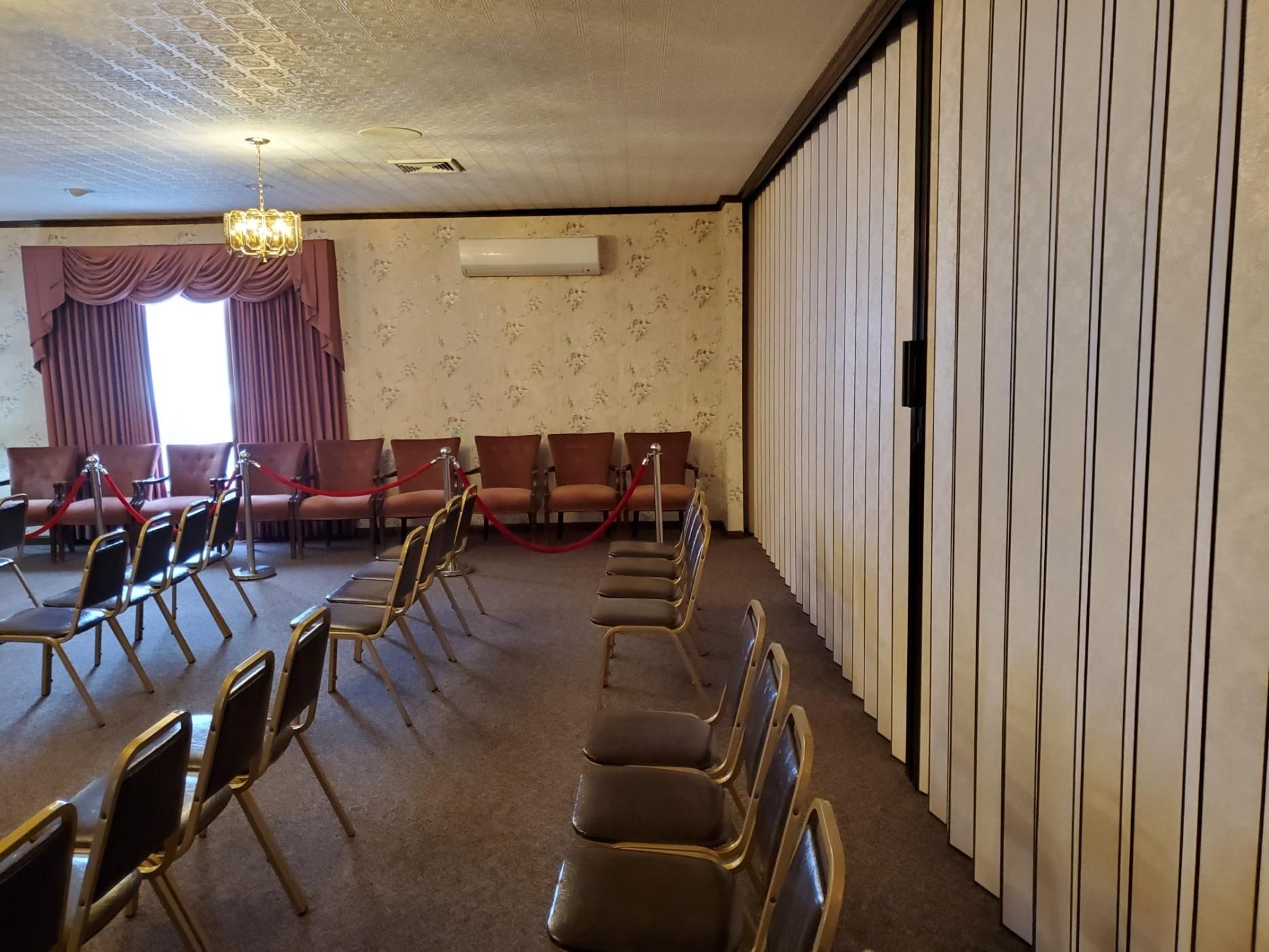 Empty meeting room with rows of chairs, striped wall panels, curtains, and a ceiling light