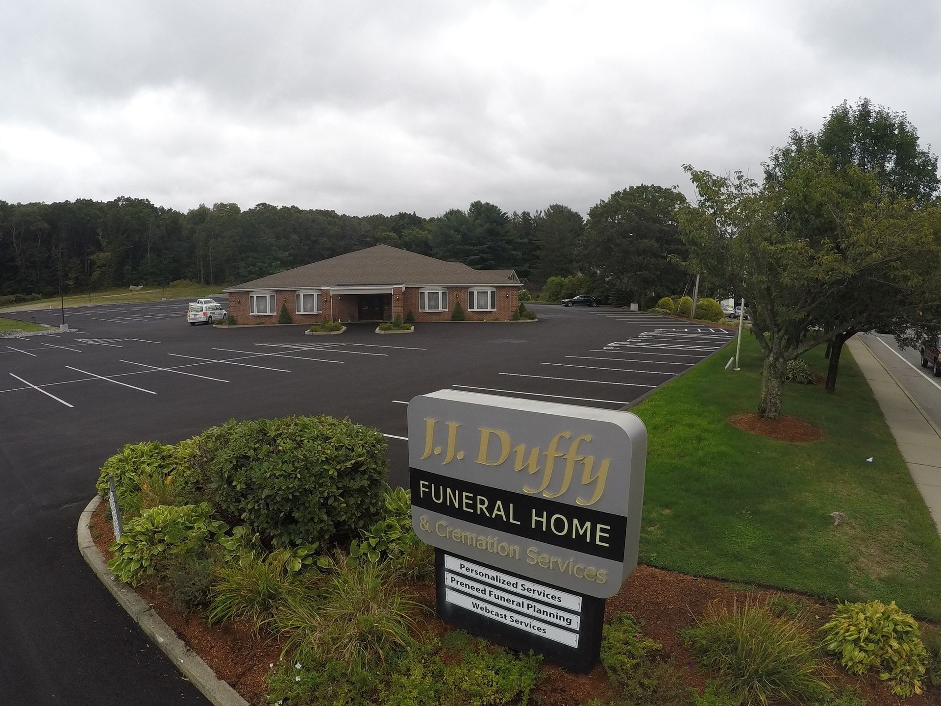 J.J. Duffy Funeral Home sign in front of a brick building with a large parking lot and trees