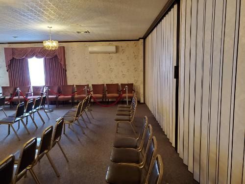 Empty meeting room with rows of chairs, a chandelier, curtains, and a wall-mounted air conditioner