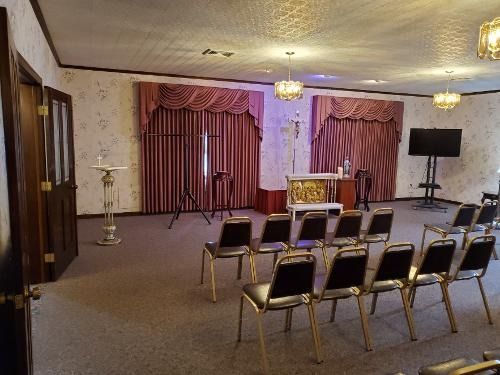 Empty hall with rows of chairs facing a curtained stage and podium, lit by ceiling chandeliers
