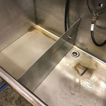 Stainless steel commercial sink with a divider; stains visible in the basin.