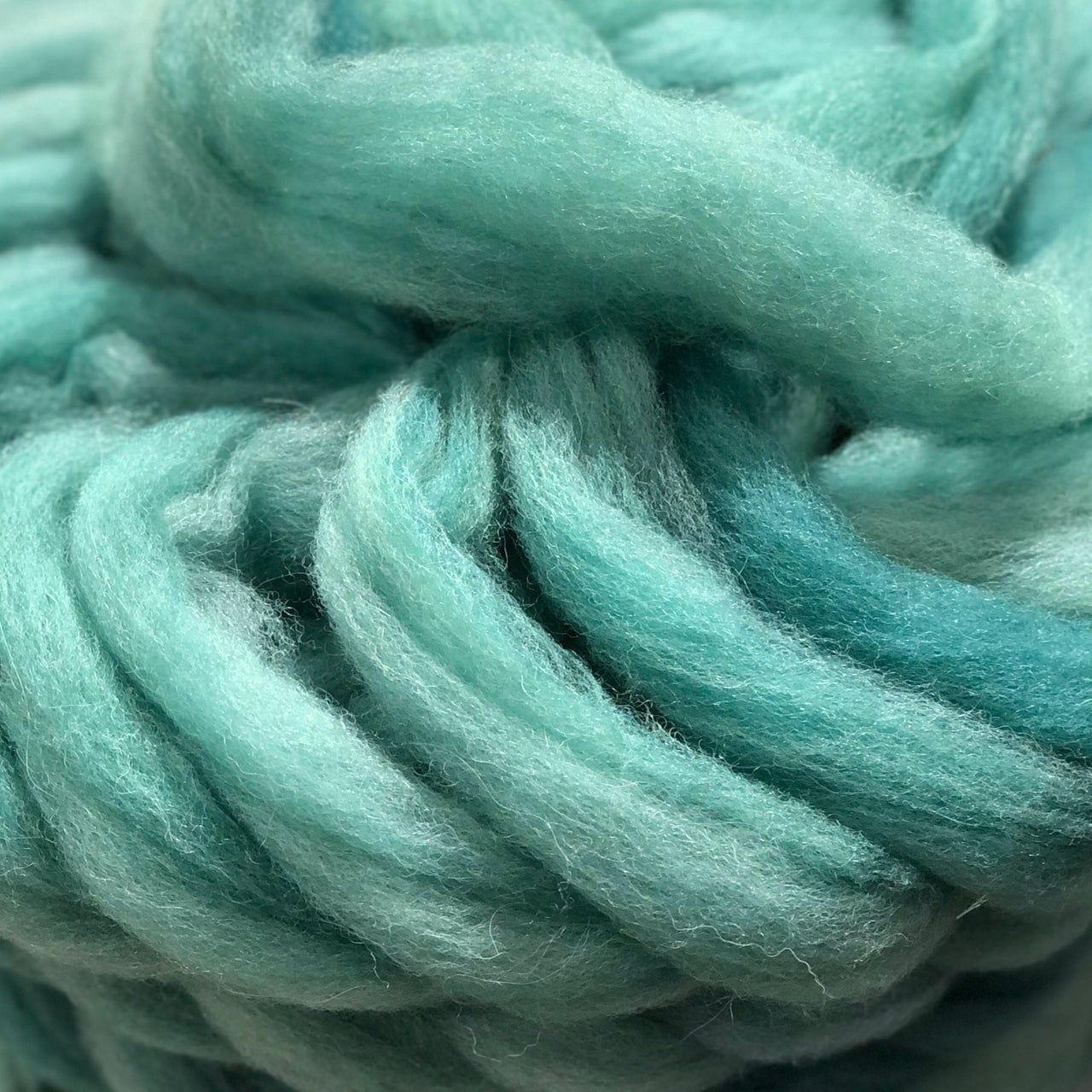 Thick, aquamarine wool roving, tightly coiled. Varying shades of blue-green create depth.