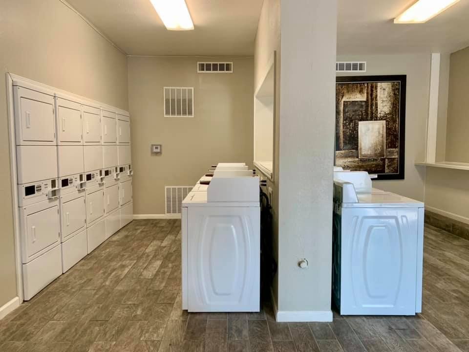 Laundry room with white washers and dryers, beige walls, and wood-look flooring.