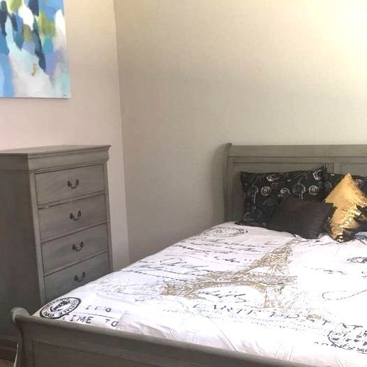 Bedroom with a gray dresser and bed with decorative pillows and Eiffel Tower design on the comforter.
