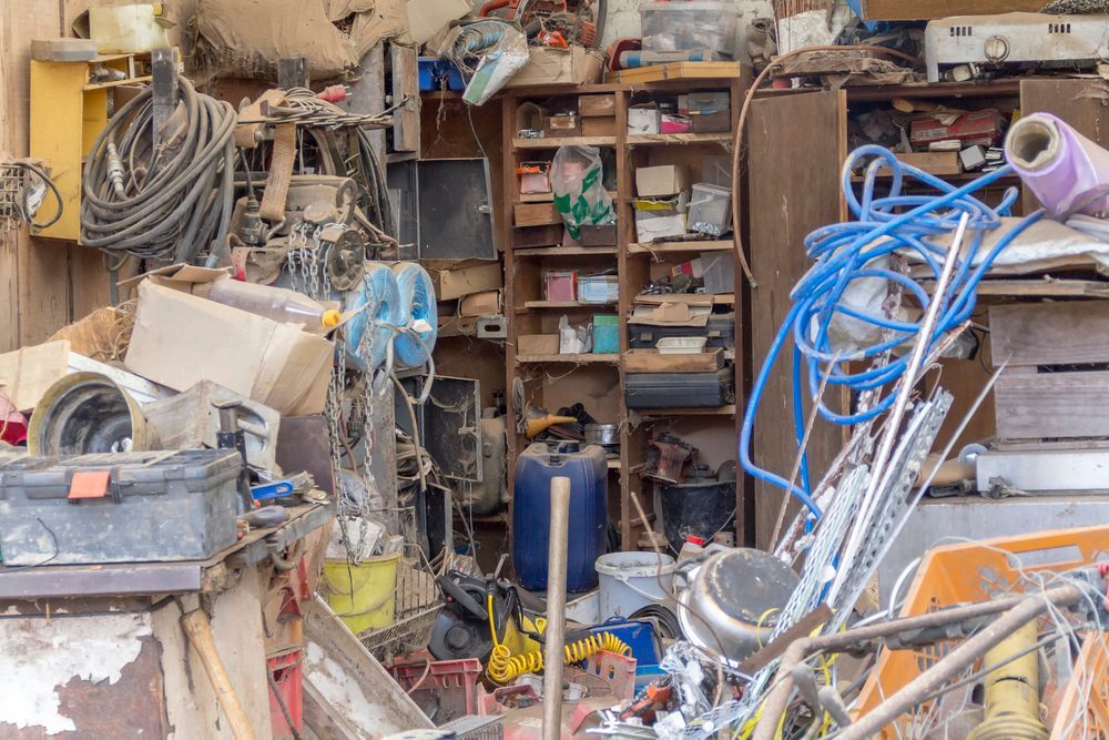 Un'officina disordinata con cavi aggrovigliati, attrezzi, scaffali e materiali accatastati in un magazzino polveroso.