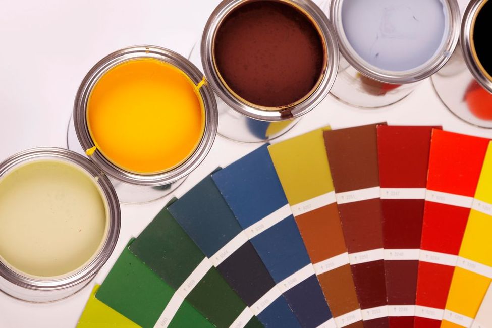 Materiali per dipingere, tra cui rulli, pennelli e campioni di colore su una superficie di legno bianca.