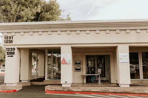 Exterior of a beige building with signage, entrance doors, and accessibility markings by the walkway