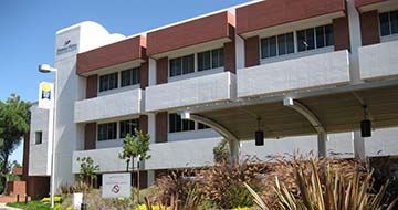 Modern building exterior with red roof, white walls, and landscaped plants under a clear blue sky