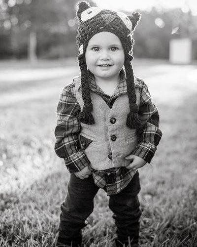 Smiling child in a plaid shirt and animal hat standing outdoors on grass