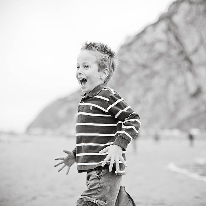 Child in a striped shirt laughing on a beach with mountains in the background