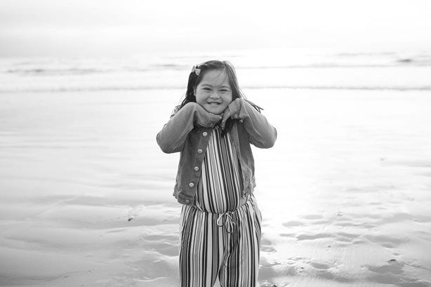 Smiling child standing on a beach, holding their cheeks, in a striped outfit