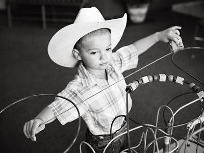 Child in a cowboy hat playing with a lasso over a wire basket indoors