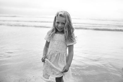 Smiling child in a light dress standing on a beach with waves in the background