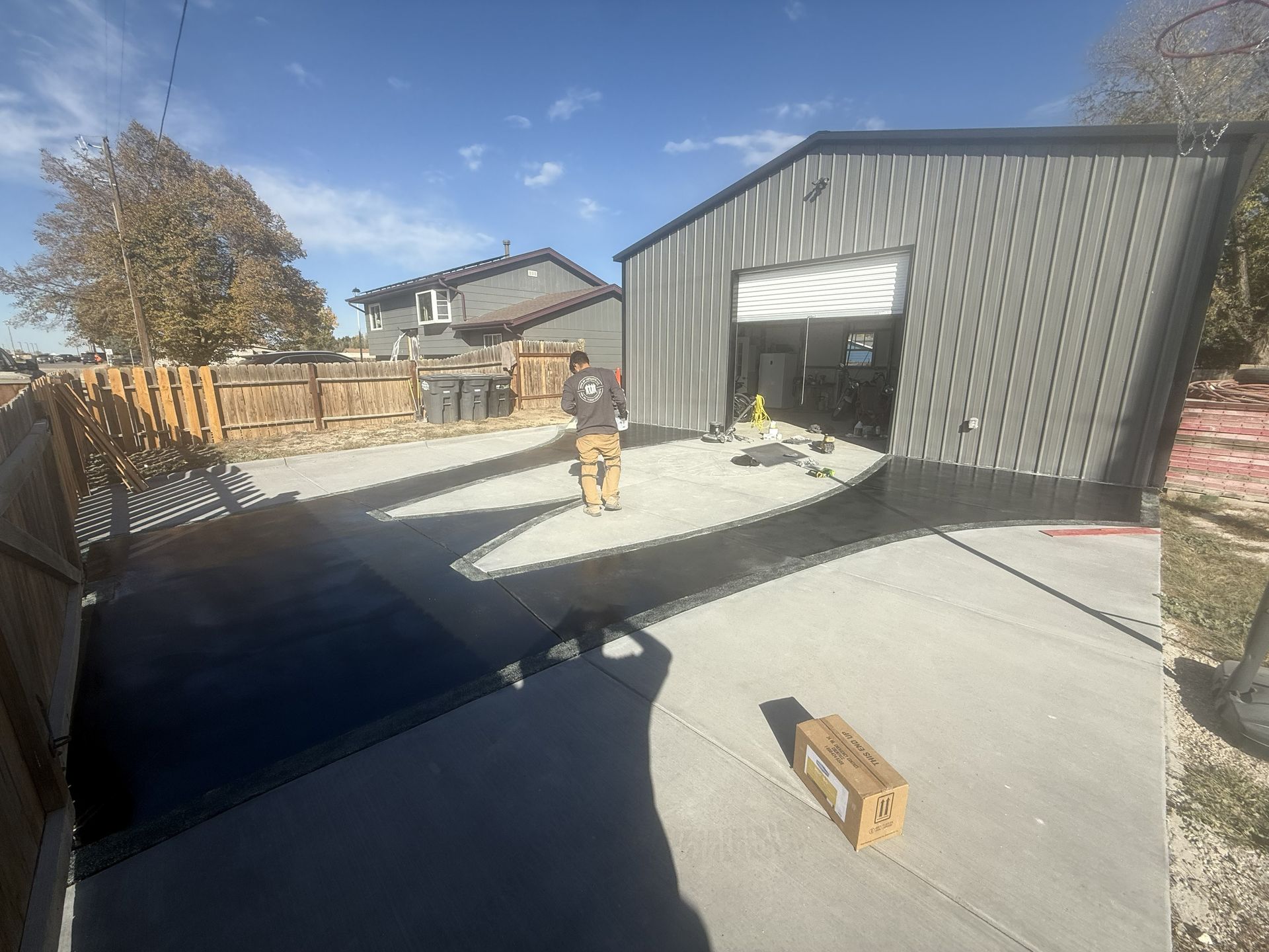 Person standing in front of a metal garage with the door open. Concrete driveway, blue sky.