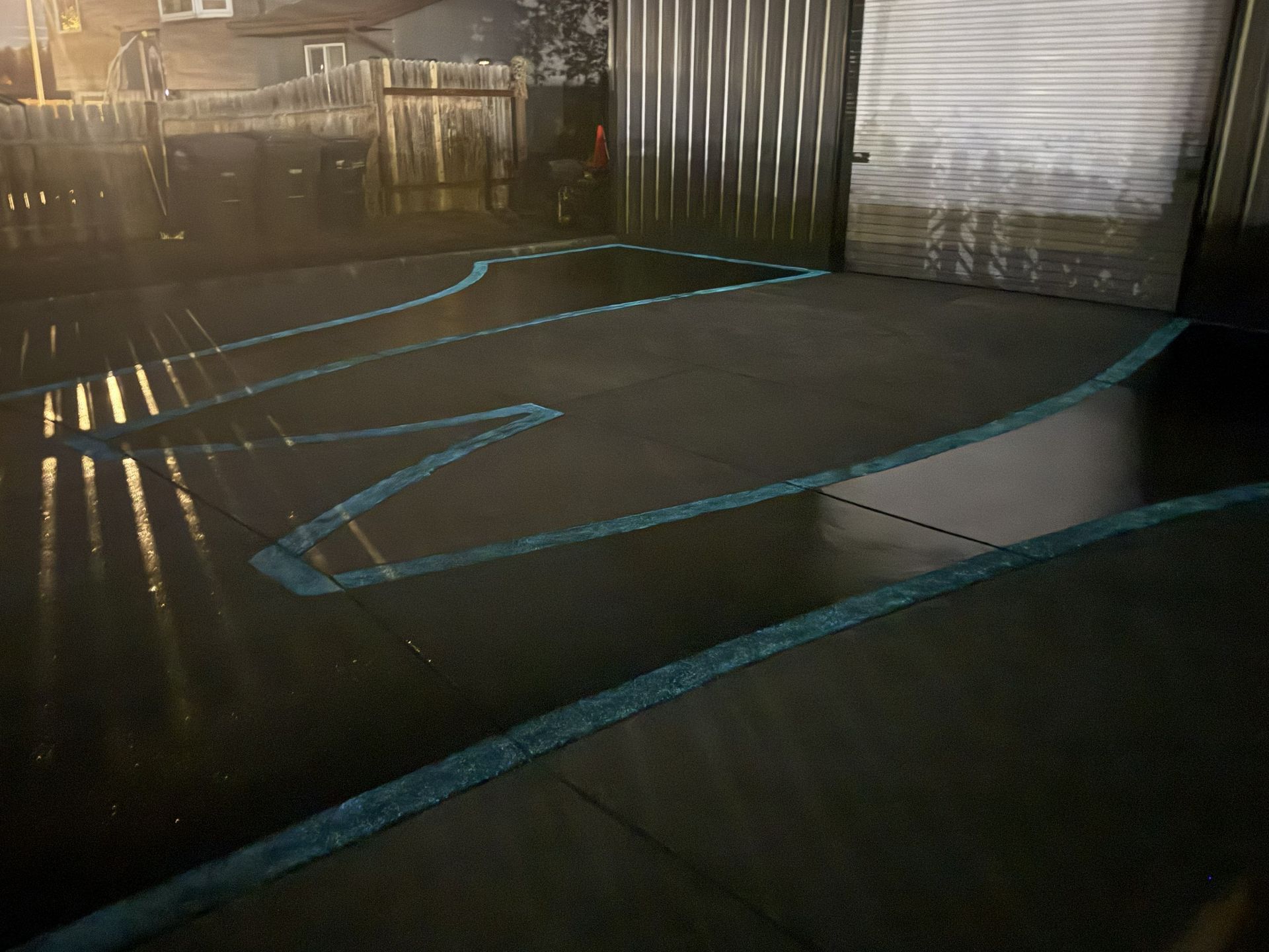 A wet, dark surface with blue chalk outline of a rocket shape, near a corrugated metal garage door.