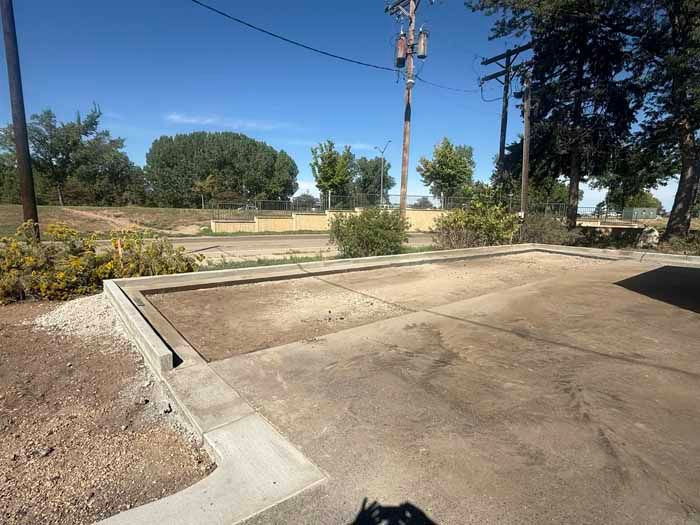 Concrete pad with a low wall, dirt area in the background, power lines, and blue sky.