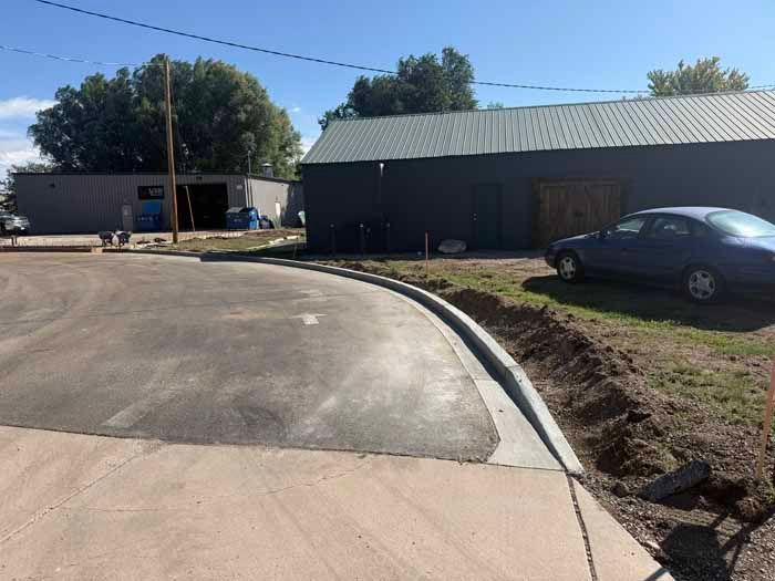 Asphalt road curves past a building with a metal roof. A car is parked to the right.