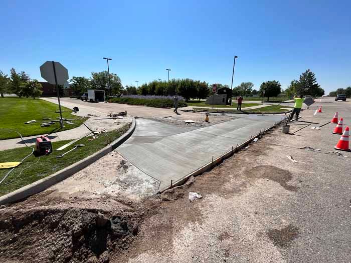 Freshly poured concrete sidewalk being constructed near a road and landscaped area; workers are present.