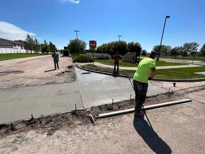Construction workers pouring and leveling concrete for a sidewalk at a road intersection on a sunny day.