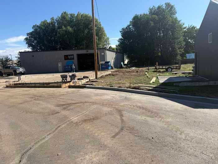 Paved street in front of industrial building with trees and blue sky.
