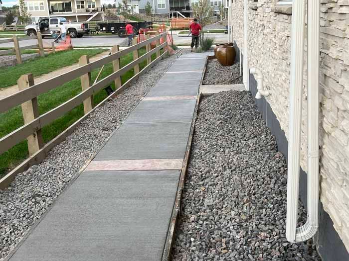 Sidewalk with gravel border next to a fence and house. A person stands nearby.