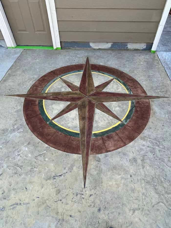Compass rose design in brown, yellow, and green on a gray concrete surface near a door.