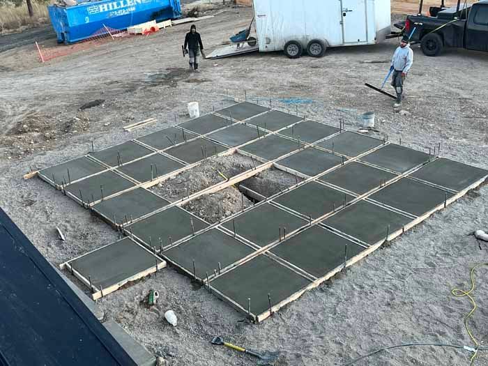Concrete slab being poured, workers on site, forms and stakes visible.