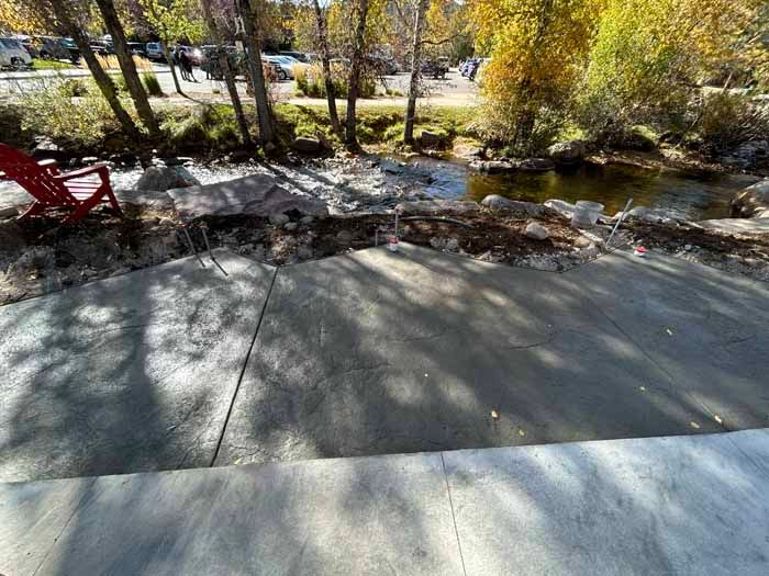 Concrete path beside a river with a red chair, trees with yellow leaves in the background.