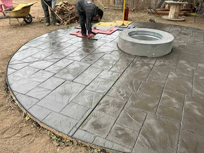Stamped concrete patio installation around a fire pit. Workers smooth the surface.