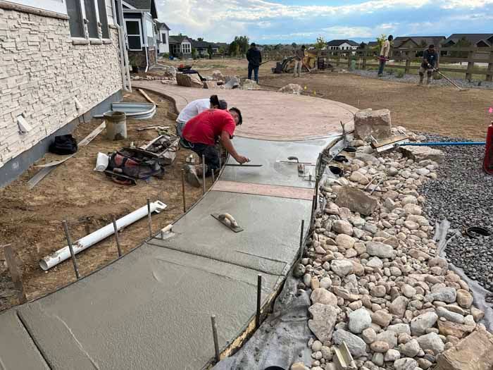Construction workers smoothing wet concrete for a pathway and patio in a residential yard.