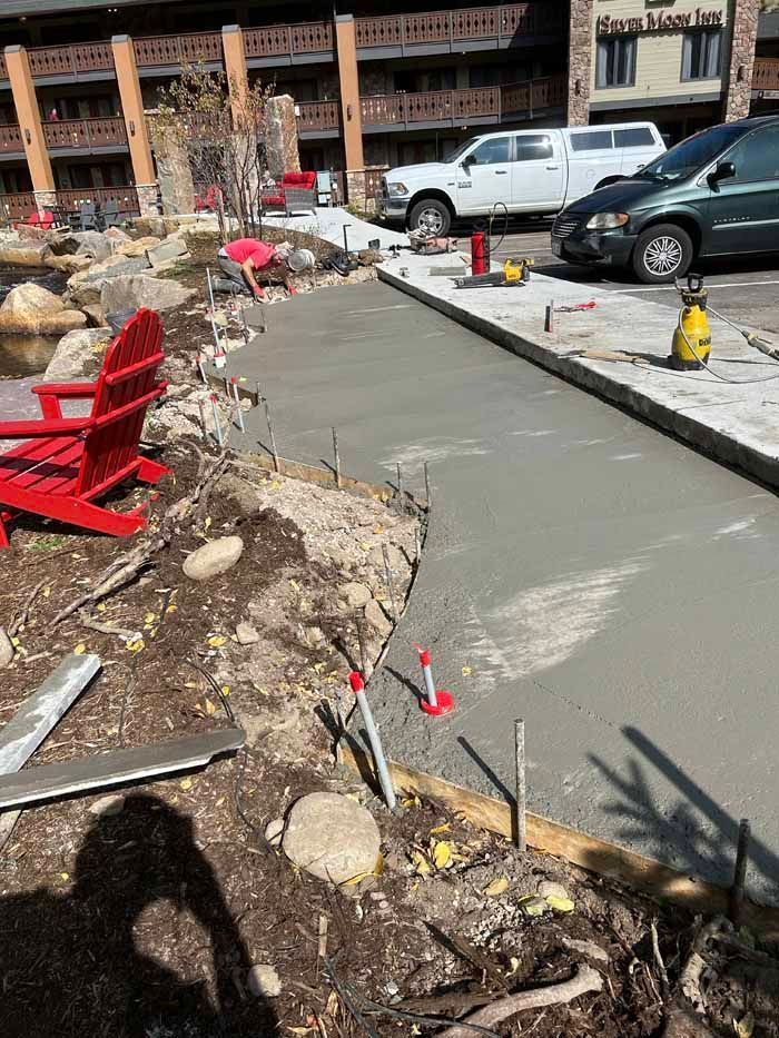 Freshly poured concrete walkway next to a landscaped area and parking lot.