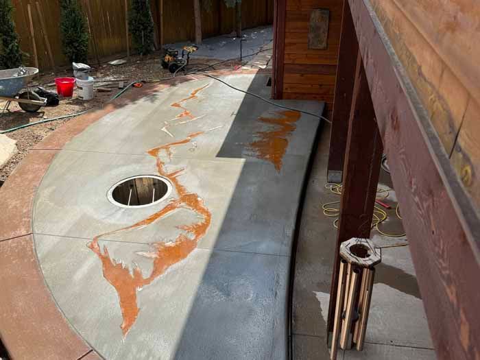 Concrete patio with brown staining, a built-in fire pit, and wooden pergola.