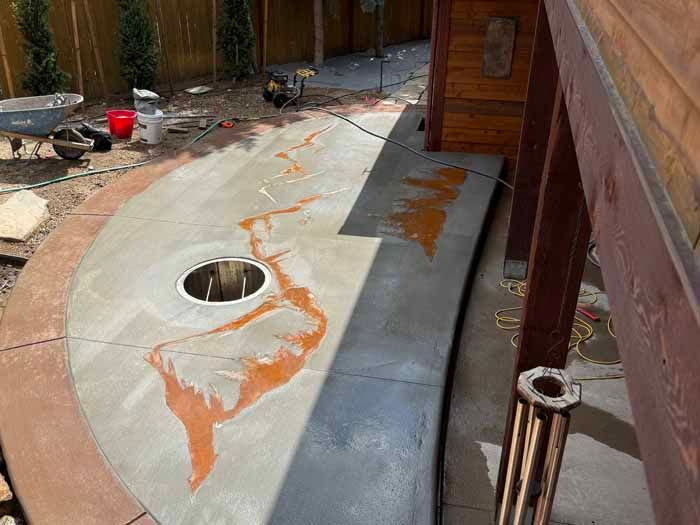 Curved concrete patio with orange stain; partially finished with tools and a wooden structure in the background.