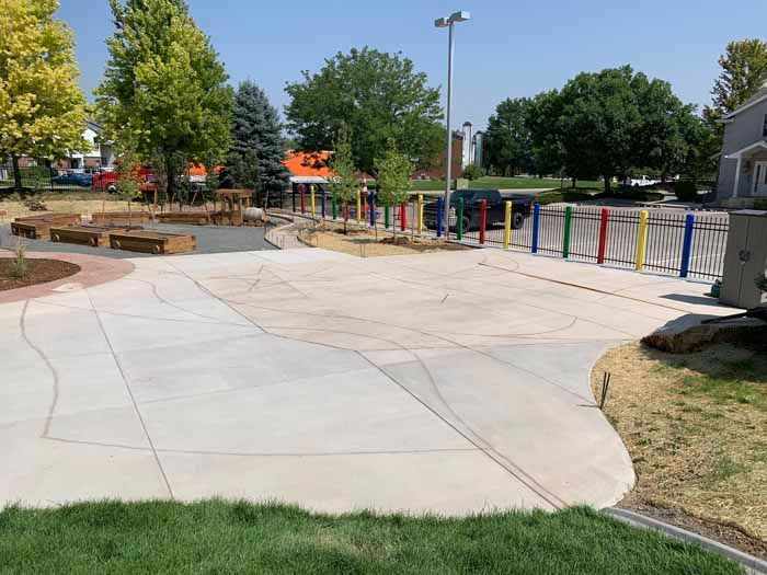 Playground with concrete path, musical instruments, trees, and grass.