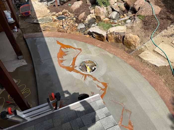Concrete pool construction with orange markings, surrounded by rocks and a hose. Ladder nearby.