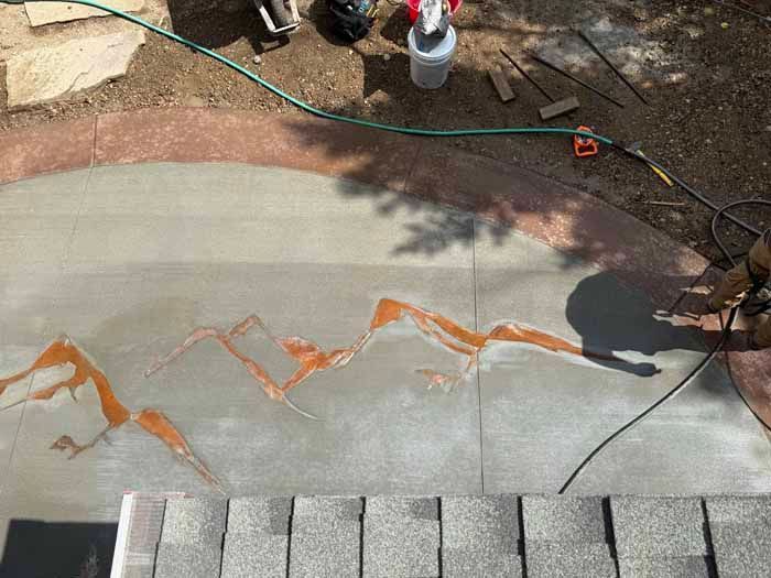 Concrete patio with orange mountain design being applied.