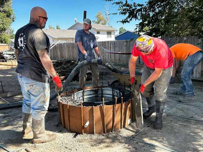 Four people pouring concrete into a round form outdoors. Construction workers in work clothes.