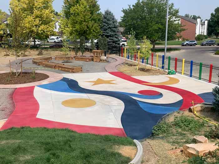 Colorful abstract playground with painted concrete, trees, and fence.
